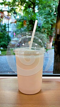 Transparent plastic glass with a milkshake and a straw on a table