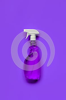 Transparent purple spray bottle with window cleaner on purple background.