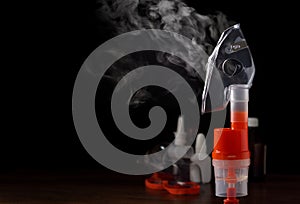 Transparent respiratory mask on atomizing cup with steam against medical equipment on black background