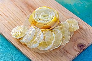 Transparent slices of lemon and peel on a cutting wooden board and blue surface. Healthy vegetarian food. Top view.