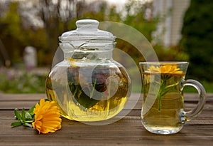 Transparent teapot and a Cup of herbal tea on a wooden table on a blurred background