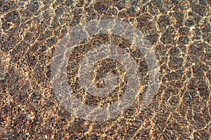 Transparent texture of sea, lake surface of clear water with ripples above sandy pebble bottom. Abstract summer background