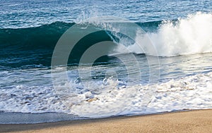 Transparent tourqouise blue wave tube breaking with foam on shoreline with backspray, and backwash