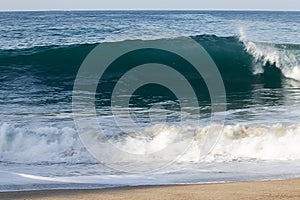 Transparent tourqouise blue wave tube breaking with foam on shoreline with backspray, and backwash