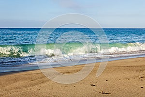 Transparent tourqouise blue wave tube breaking with foam on shoreline