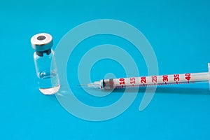 Transparent vial container with liquid medicine near small insulin syringe with capacity 1 CC and small needle on blue background photo