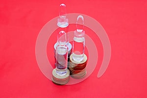 Transparent vials with the drug are on the coins on a red background. Illustration of the cost of pharmaceuticals. For use in pres