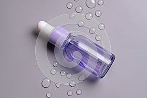 Transparent violet cosmetic bottle with pipette on grey background with water drops, product packaging, anti aging serum with