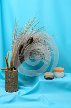 Transparent and white jars with cream for hand and face skin care on the background of an autumn bouquet of reeds