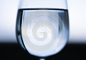 Transparent wine glass with water with reflection, small bubbles. Blue black white blurred background