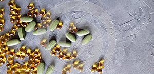 Transparent yellow gel capsules and green tablets on a grey concrete background. The concept of a healthy lifestyle