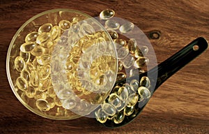 Transparent yellow pills in bowl on background of wood, omega 3.