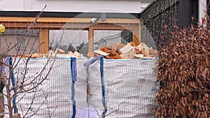 Transport bags on pallets with birch firewood standing on the sidewalk in front of a villa.