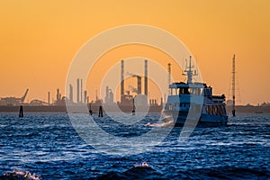 Transport boat leaving the petroleum refinery during sunset