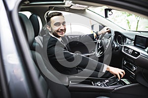 Transport, business trip, destination and people concept - close up of young man in suit driving car look at camera