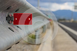 Transport highway infrastructure concept photography of red road reflector on metal side fence with unfocused background