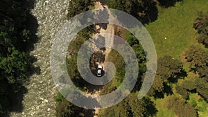 Transport white sedan car moving on dirt road through wooded area. Aerial view