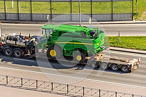 Transportation of harvester John Deere S760i loaded onto cargo platformon highway in the city. Russia, Saint-Petersburg. 22 may