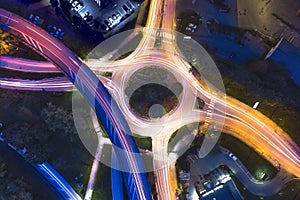 Transportation at night with commuting vehicle traffic creating light trails on the road with motion blur, roundabout and motorway