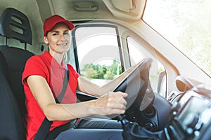 Transportation services - young female driver in red uniform driving a van. smiling at camera