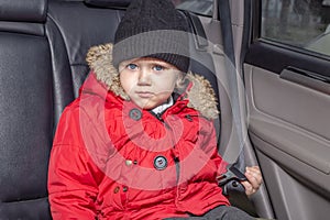 Transportation of small children in the car. A boy in a red jacket sits in the passenger compartment of a car not