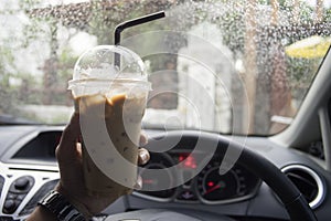 Transportation and vehicle concept - hand of man holding a take away cup of iced coffee while parking the car with water drop