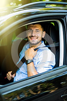 Transportation and vehicle concept. Young man fastening seat belt in car