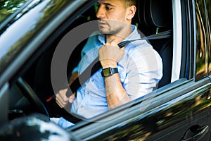 Transportation and vehicle concept. Young man fastening seat belt in car