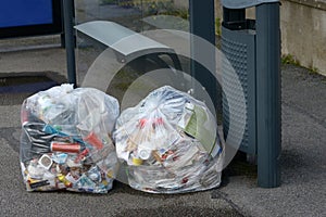 Trash bags placed next to the garbage can at a bus stop