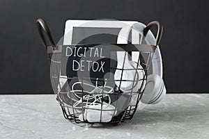 Trash bin with different gadgets and words DIGITAL DETOX on light grey marble table photo