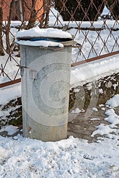 Trash bin at the entrance gate. Metal container covered with snow