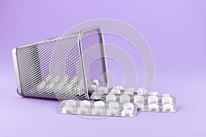 Trash bin with packs of white capsules and pills packed in blisters with copy space on purple background. Focus on foreground, sof