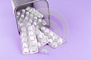 Trash bin with packs of white capsules and pills packed in blisters with copy space on purple background. Focus on foreground, sof