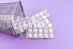 Trash bin with packs of white capsules and pills packed in blisters with copy space on purple background. Focus on foreground, sof