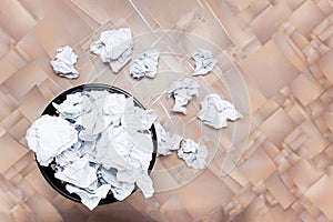 A trash can filled with crumpled papers stands on a wooden floor.