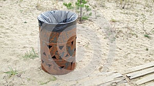Trash can made of rusty metal barrel with plastic bag on the sand at the beach