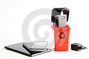 Trash can and many recyclable gadgets, smartphones, power bank, tablet and power supply on a white background. The problem of