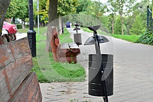 The trash can is round between the benches in the park.