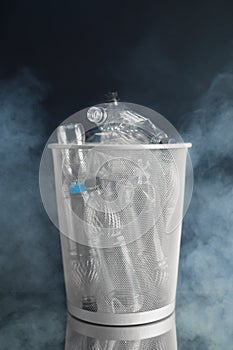 Trash can with wasted plastic bottles, black background with smoke, pollution concept