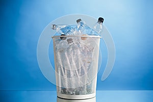 Trash can with wasted plastic bottles, blue background