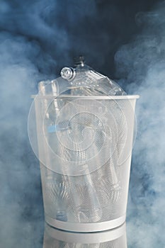 Trash can with wasted plastic bottles, smoke background, pollution concept