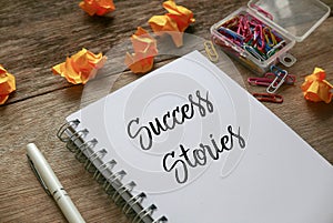 Trash paper, paper clips,pen and notebook written with Success Stories on notebook on wooden background photo