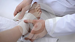 Traumatologist applying bandage to sprained ankle, workout injury, leg closeup photo