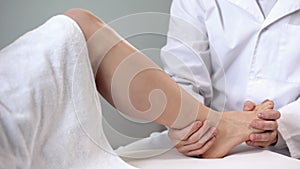 Traumatologist moving patient ankle, assessing severity of injury, closeup photo