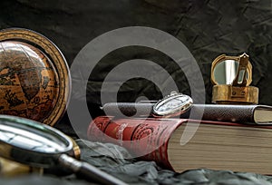 Travel or adventure concept background. Pocket watch, binoculars, antique compass, globe, magnifying glass and stack of books on