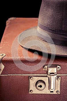 Travel and adventure concept. Vintage brown suitcase with vintage hat on black background