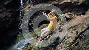 Travel adventure woman taking photos of a smartphone on a mountain waterfall, enjoying the beautiful scenery of nature