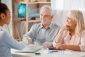 Travel agent at office sitting shaking hands with senior client cheerful