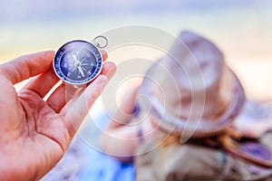 Travel around the world: compass in foreground, beautiful girl with straw hat lying on the beach in the background