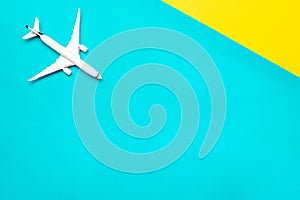 Travel background. White toy airplane, aircraft on bright blue and yellow backdrop. Flight or fly in sky air plane